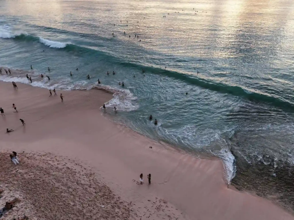 Beachgoers swimming and relaxing along a sandy shoreline at sunset.