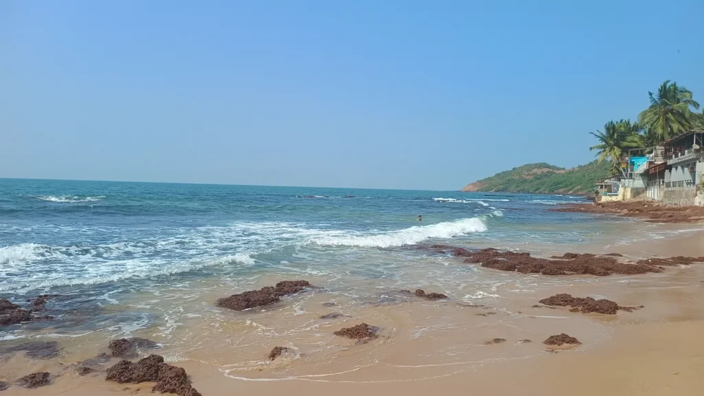 Sandy beach in India with blue sea waves, rocky shoreline, palm trees, and beachside buildings.