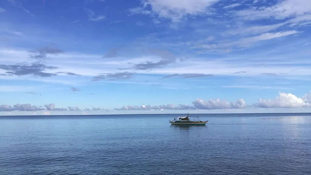 Small boat floating on calm blue ocean beneath a cloudy sky.
