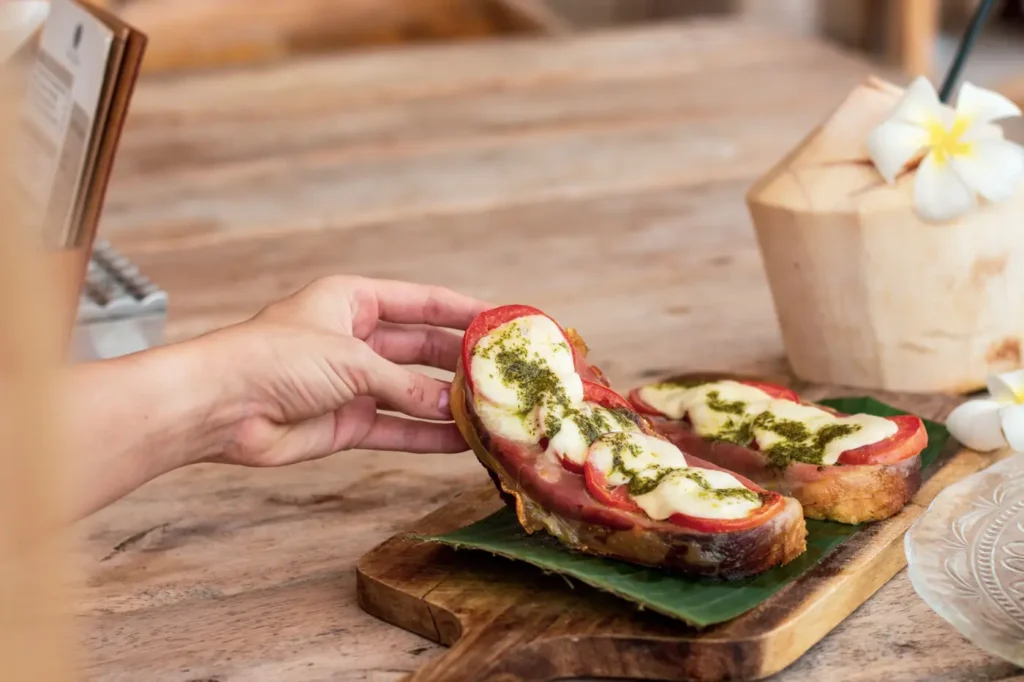Hand holding a caprese toast with melted cheese and tomatoes.