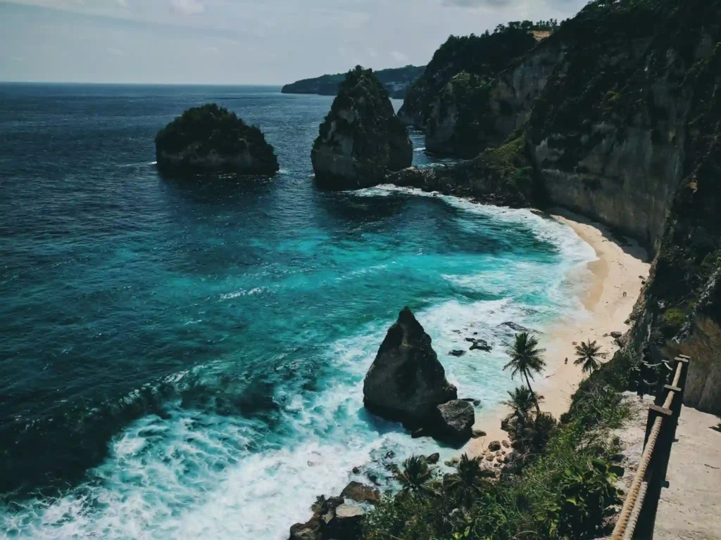 Turquoise bay with dramatic cliffs, rock formations, and a secluded white-sand beach. 