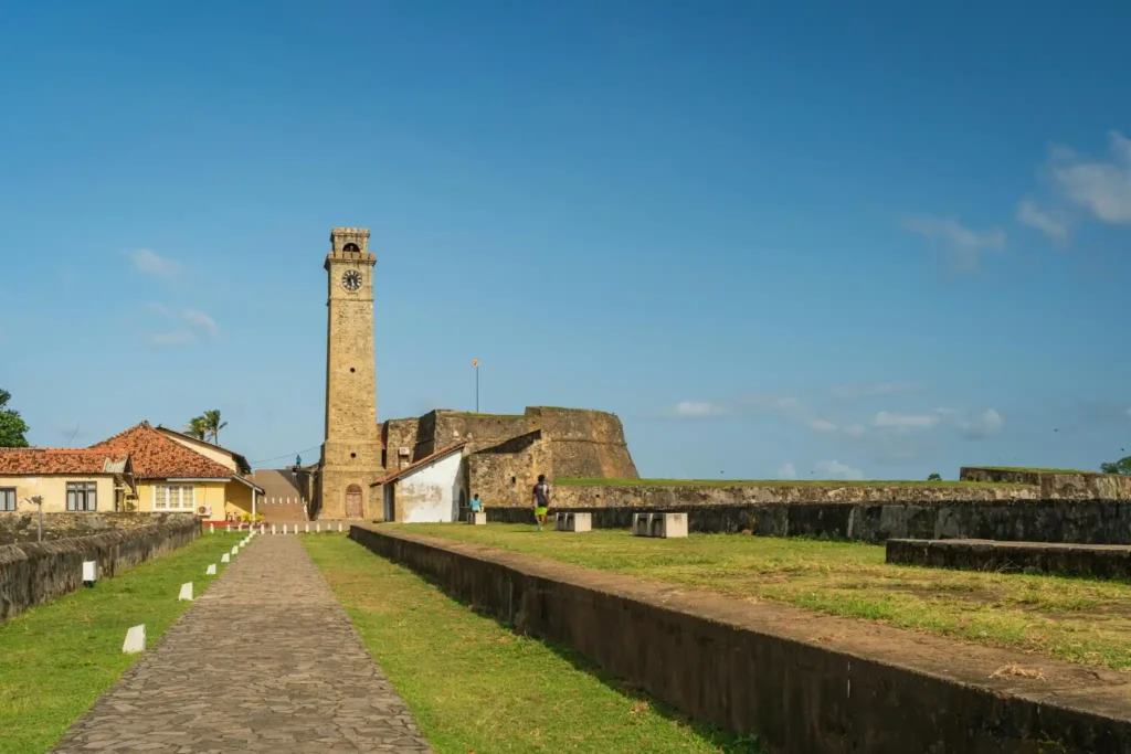 Galle Fort clock tower with stone pathway, old walls, green lawns, and blue sky in Sri Lanka. 