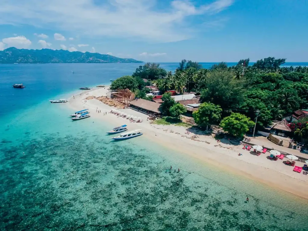Aerial view of Gili Islands beach with clear turquoise water, white sand, boats, and tropical trees.