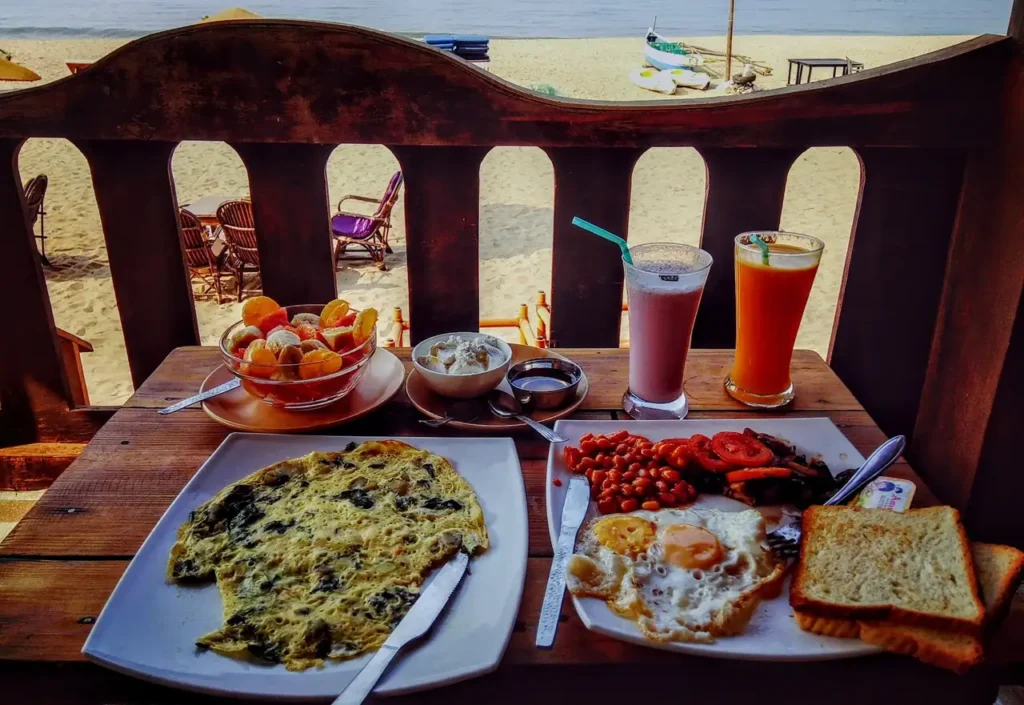 Beachside breakfast with omelet, toast, fruit, and fresh drinks overlooking the sandy shore at Goyambokka Beach.
