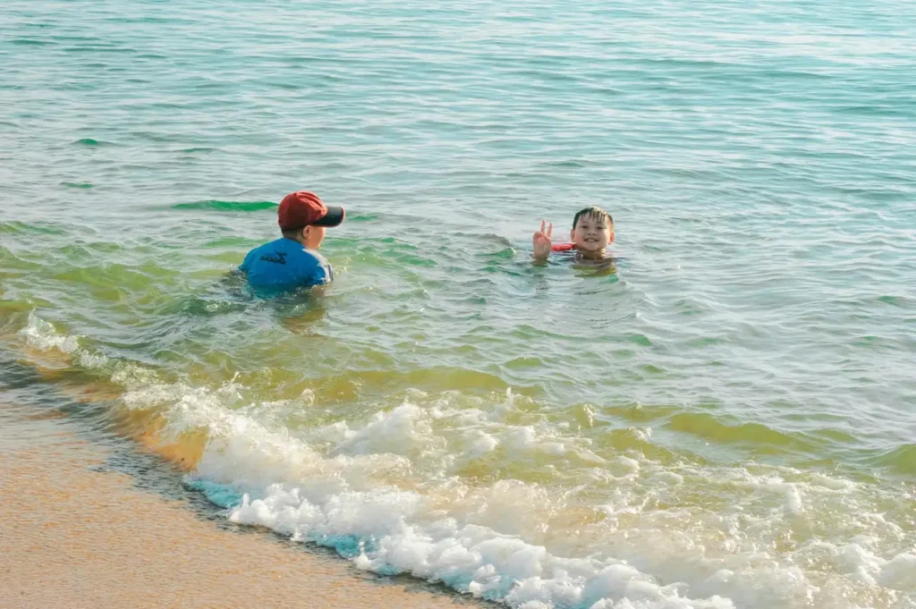 Children swimming in calm shallow sea water near the shore at Goyambokka Beach.