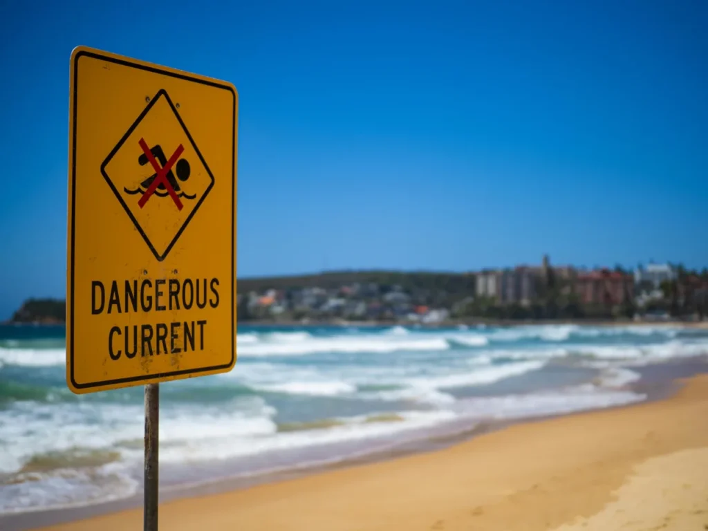 Dangerous current warning sign on a beach with waves in the background, showing unsafe swimming conditions near Goyambokka Beach.