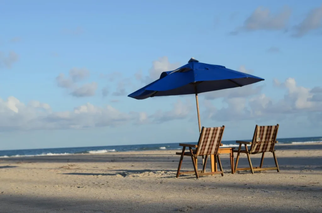 Two beach loungers under a blue umbrella on a quiet sandy beach near Goyambokka Beach. 