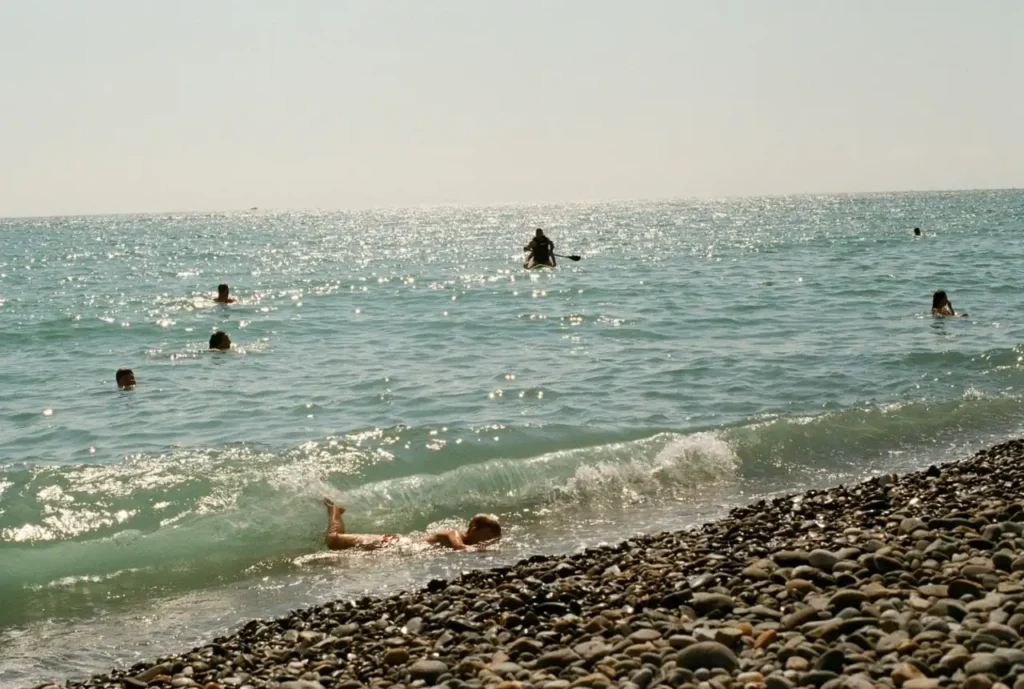 People swimming in sparkling sea water beside a pebble shoreline near Goyambokka Beach.