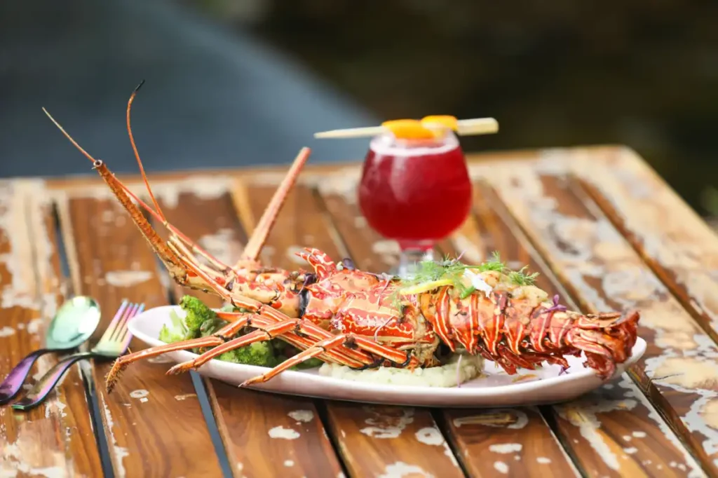 Grilled lobster served on a plate with vegetables and a tropical drink.