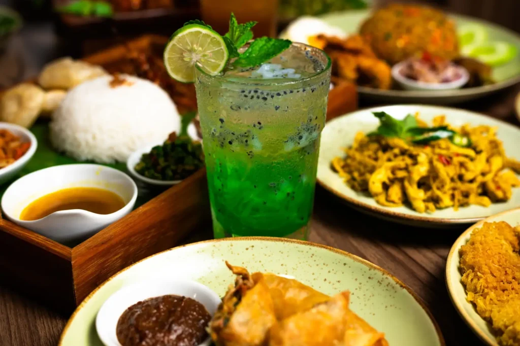 Indonesian meal with green drink, rice, and traditional dishes on a table.