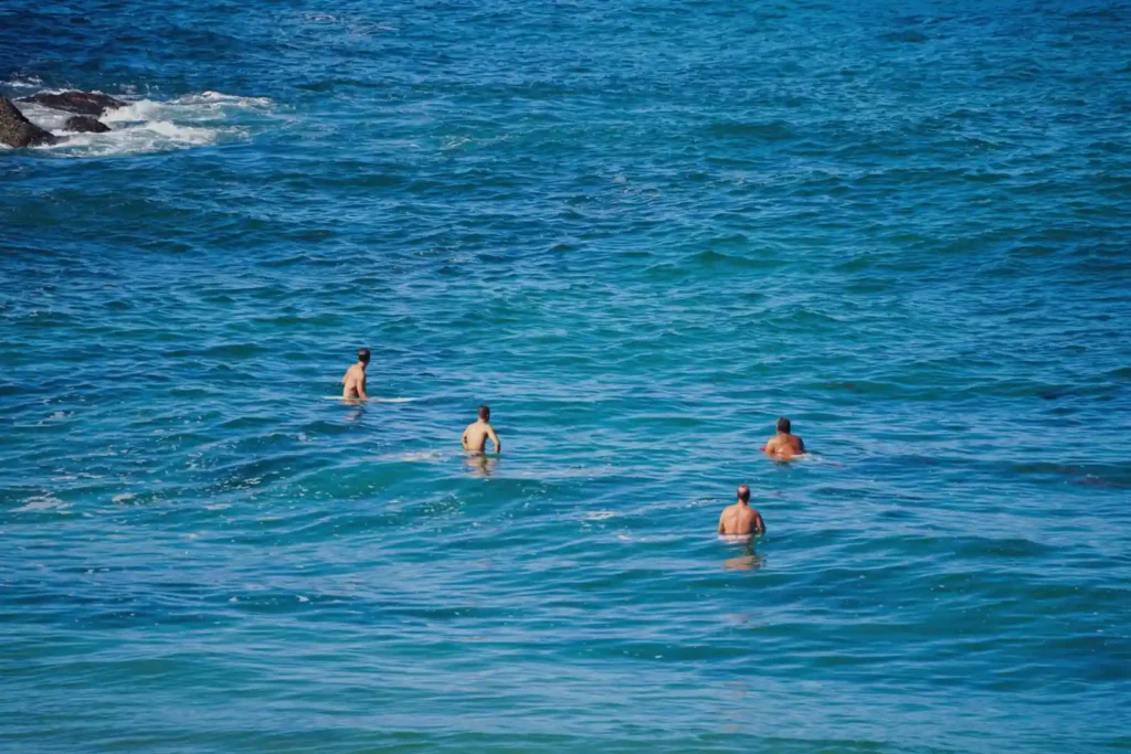 Tourists swimming in the waters of Kelingking Beach, Nusa Penida, Bali, despite the beach's strong currents and safety risks.