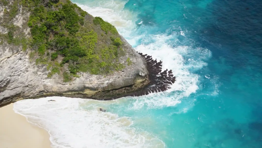 Turquoise waves crashing against rocky cliffs at Kelingking Beach.