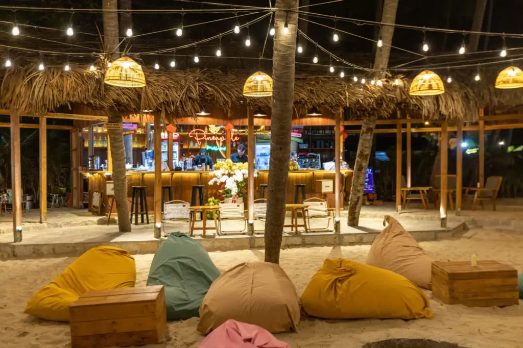 Cozy Koh Lipe beach bar at night with string lights, beanbag seating, palm trees, and a warmly lit tropical counter. 