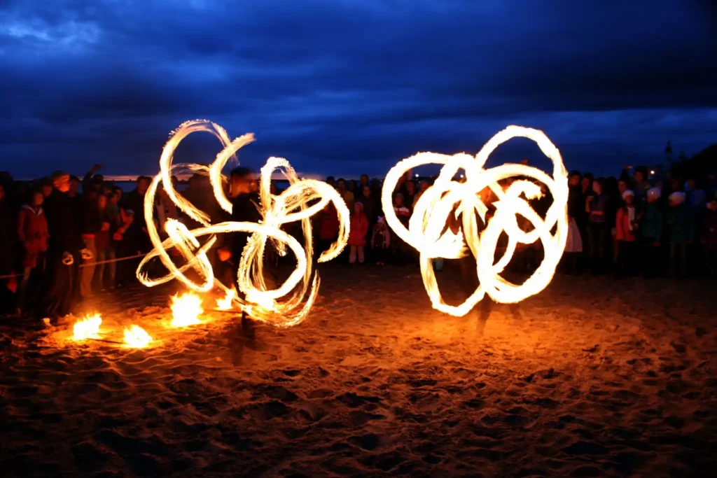 Fire performers creating bright flame trails on a beach at night as a crowd watches the Koh Lipe nightlife show.