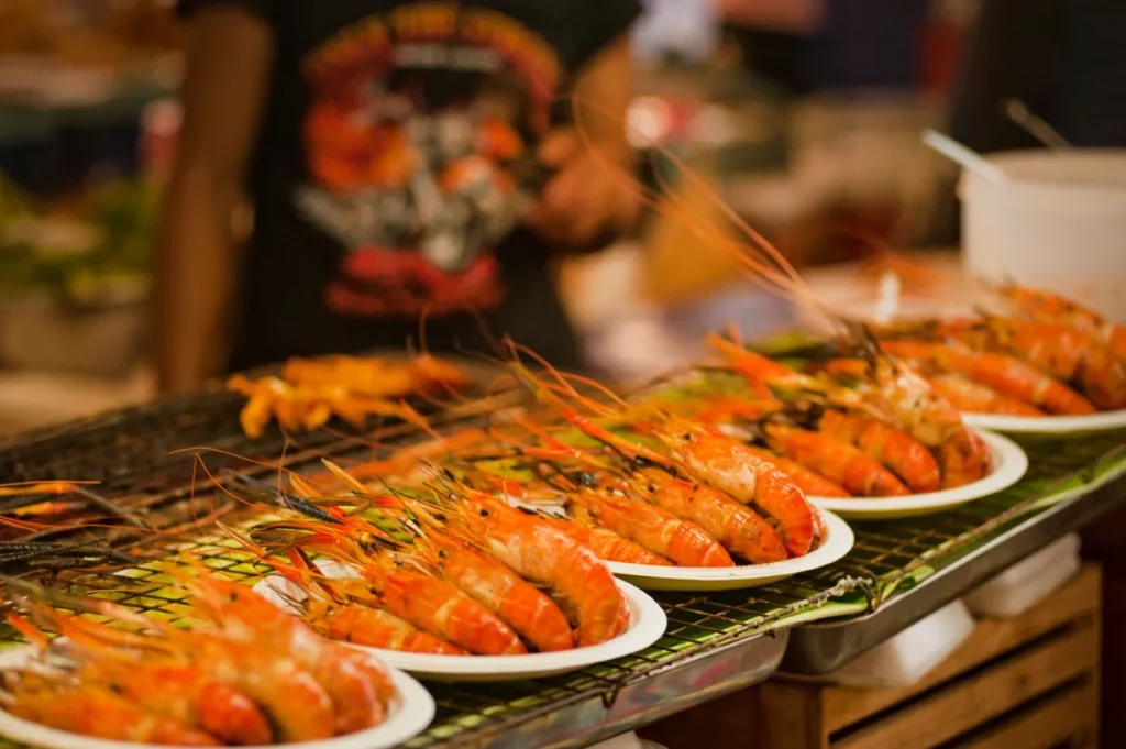 Grilled prawns served on plates at a warm night food market seafood stall.