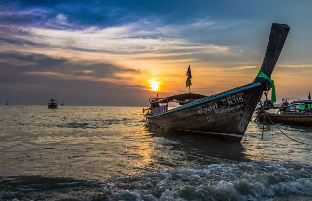 Traditional Thai longtail boat floating near Koh Lipe at sunset with golden reflections across the sea. 