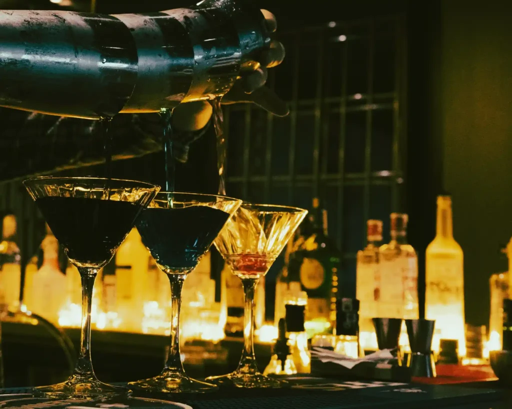 Bartender pouring cocktails into martini glasses at a warmly lit nightlife bar in Koh Lipe.