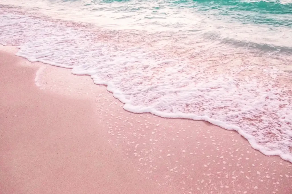 Close-up of soft pink sand on a Lombok beach with gentle ocean waves and white sea foam washing ashore.