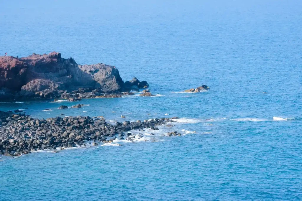 Rocky hidden coastline in Lombok with blue ocean waves, rugged cliffs, and a quiet remote shore.