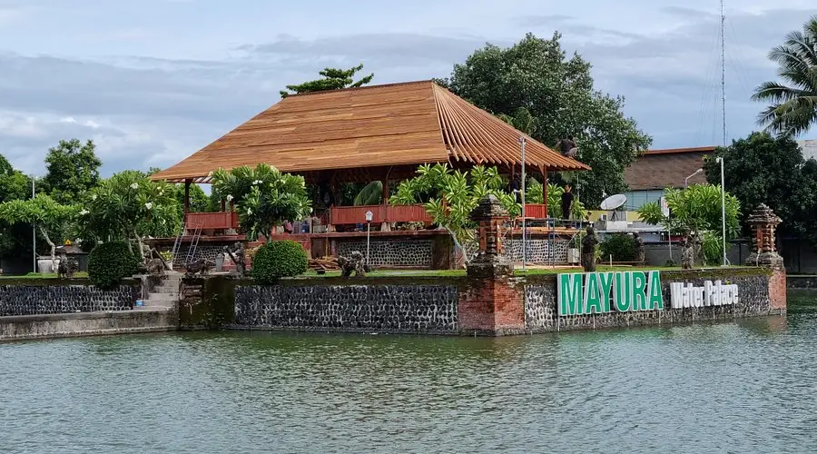 Mayura Water Palace in Lombok with a traditional wooden pavilion, garden, and pond in front.