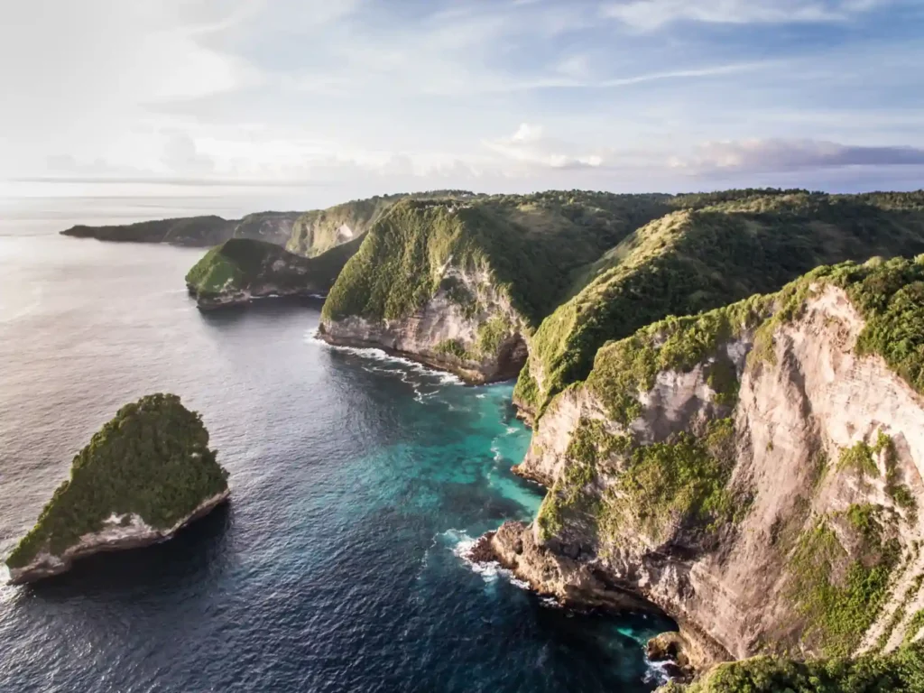 Aerial view of Nusa Penida's green cliffs and turquoise coastline. 