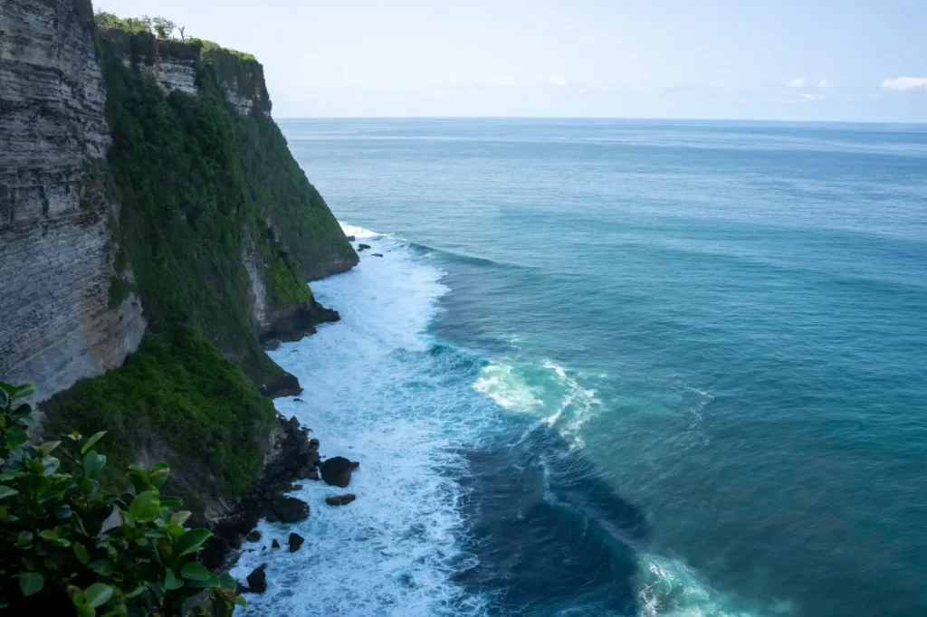 Ocean waves rolling beneath towering green coastal cliffs viewed from above