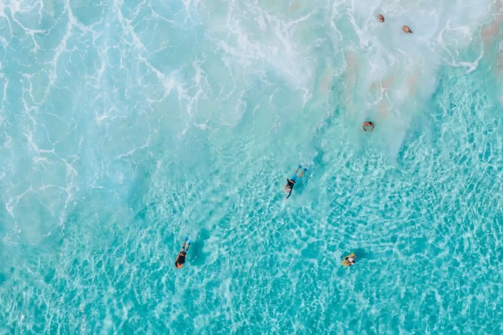 Aerial view of swimmers in clear turquoise ocean water.