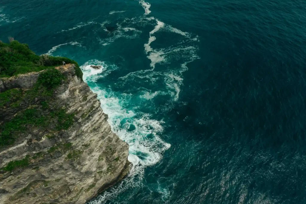 Aerial view of rocky sea cliffs and turquoise ocean.