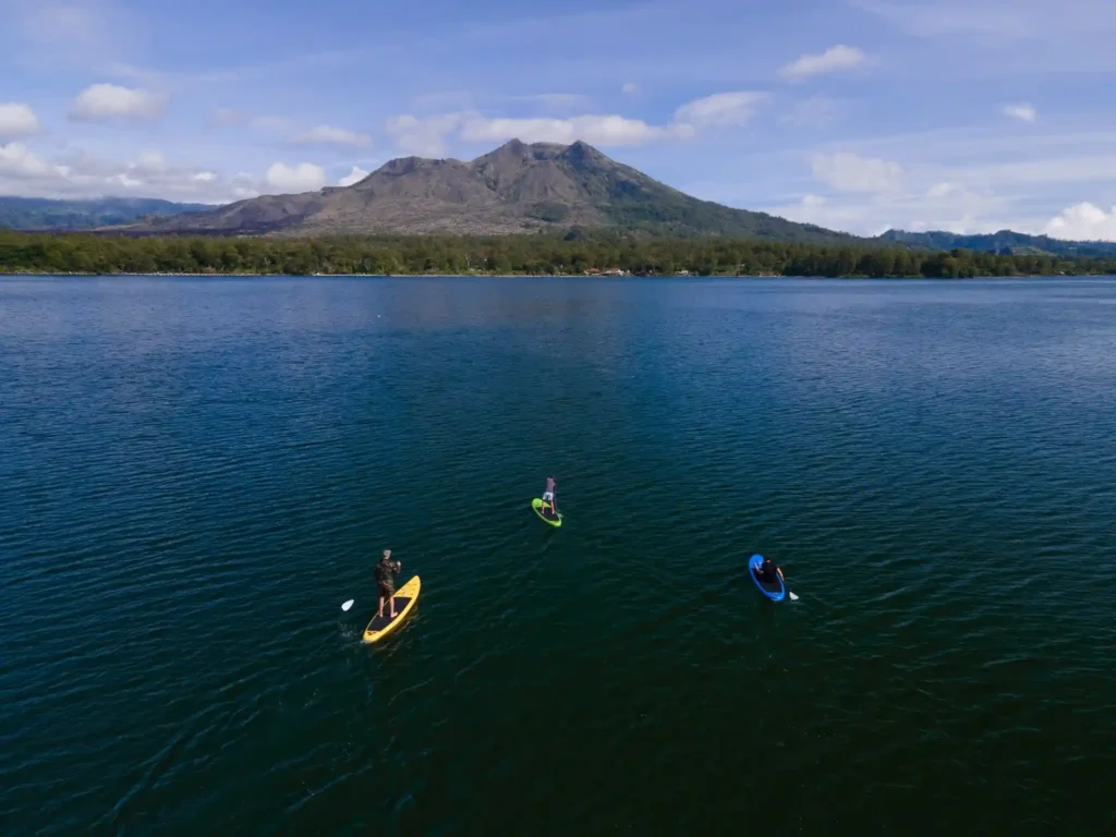 Three people paddleboarding across a calm lake with a large mountain and forested shoreline in the background.