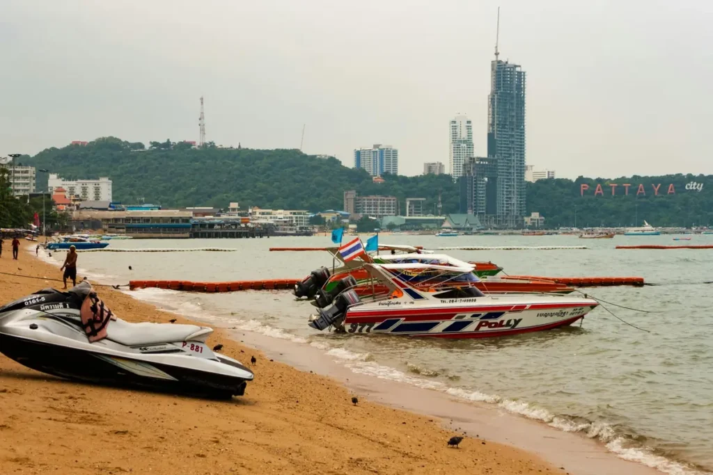 Pattaya Beach with speedboats, jet ski, city skyline, calm water, and sandy shore in Thailand.