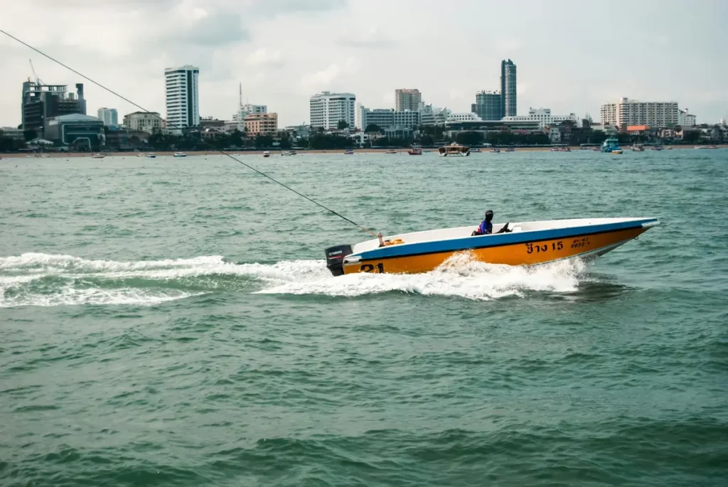 Yellow speedboat crossing green sea water with a coastal city skyline in the background.