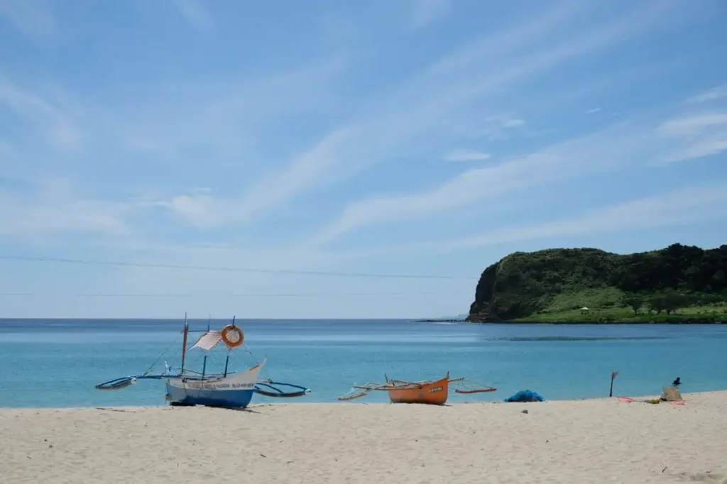 Traditional fishing boats resting on a quiet white-sand beach beside calm turquoise water.