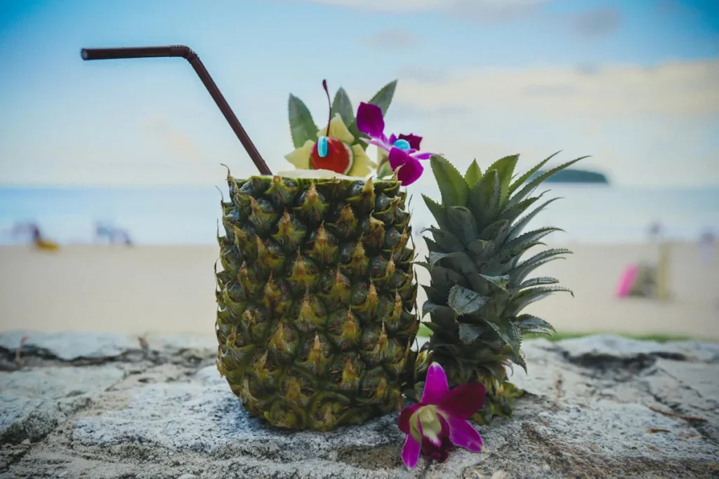 Pineapple cocktail with tropical flowers on a beach, with soft ocean and island views in the background