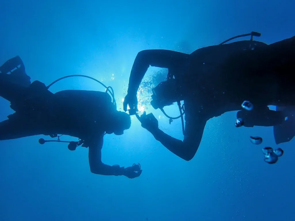 Two scuba divers underwater in blue ocean light with bubbles and diving gear silhouettes.