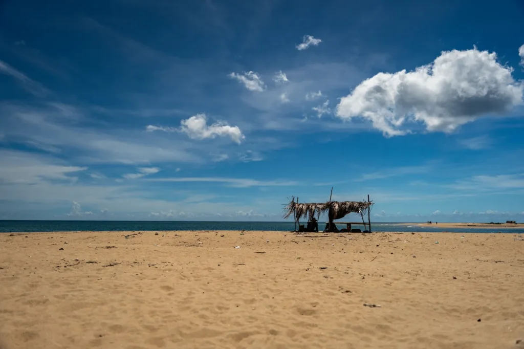 Remote sandy beach in Sri Lanka with a small palm hut, blue sky, clouds, and calm ocean views.