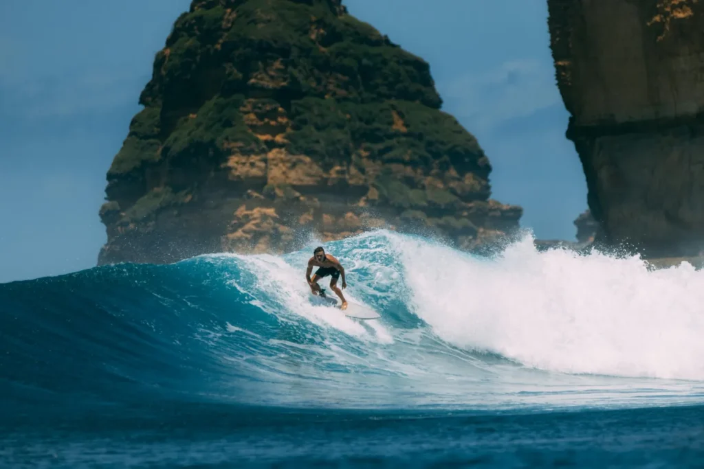 Surfer riding a powerful turquoise wave with rocky cliffs in the background.