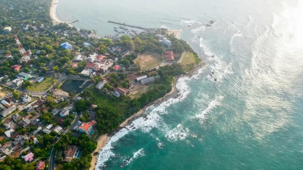 Aerial view of Tangalle coastline with turquoise ocean, rocky shore, sandy beaches, green trees, and coastal town buildings.
