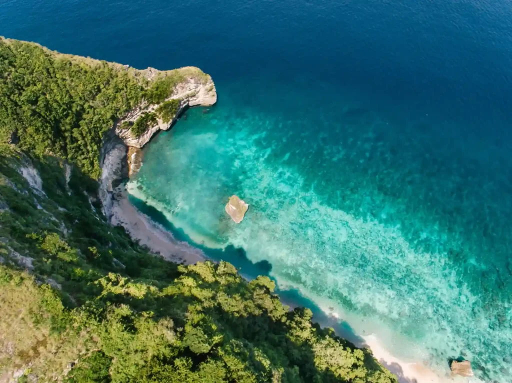 Aerial view of a secluded turquoise cove with steep green cliffs.