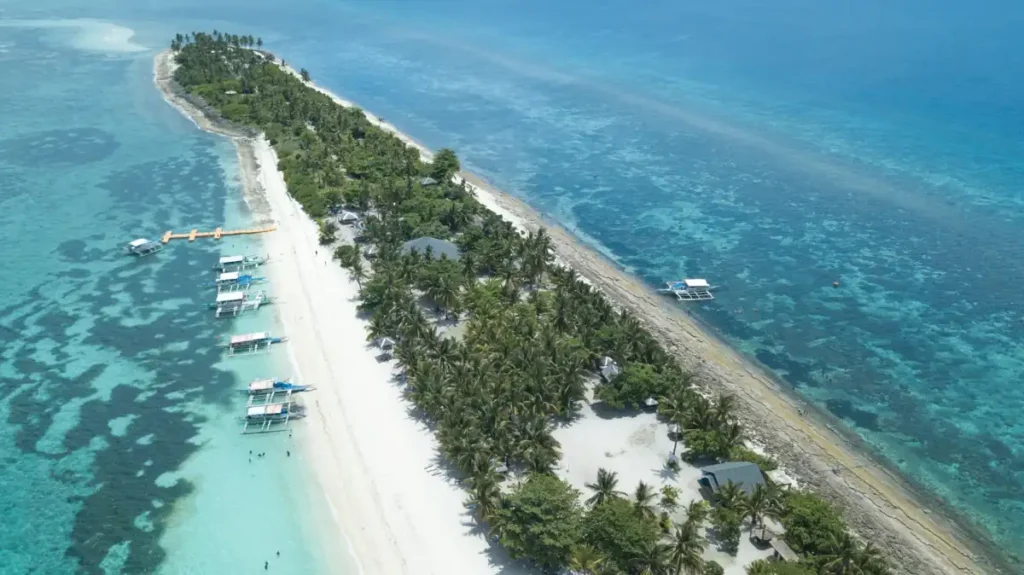 Aerial view of a tropical island with white-sand beaches, palm trees, and turquoise coral waters.