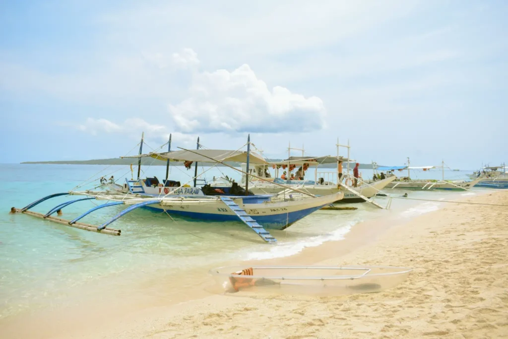 Traditional Filipino outrigger boats anchored along a white sand beach with crystal-clear turquoise water in the Philippines.