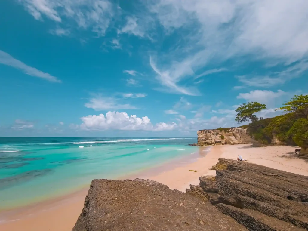 Tropical beach with turquoise water, white sand, and limestone cliffs under a bright blue sky in Bali, Indonesia.