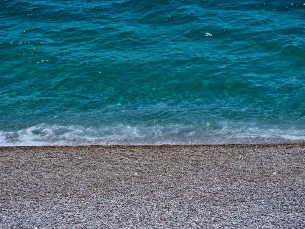 Clear turquoise waves washing onto a pebble beach shoreline.
