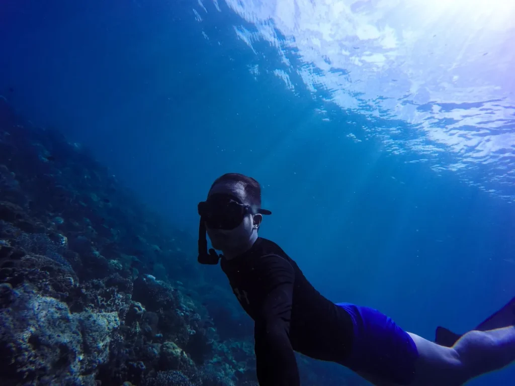 Underwater snorkeler swimming above a coral reef in clear blue tropical sea.