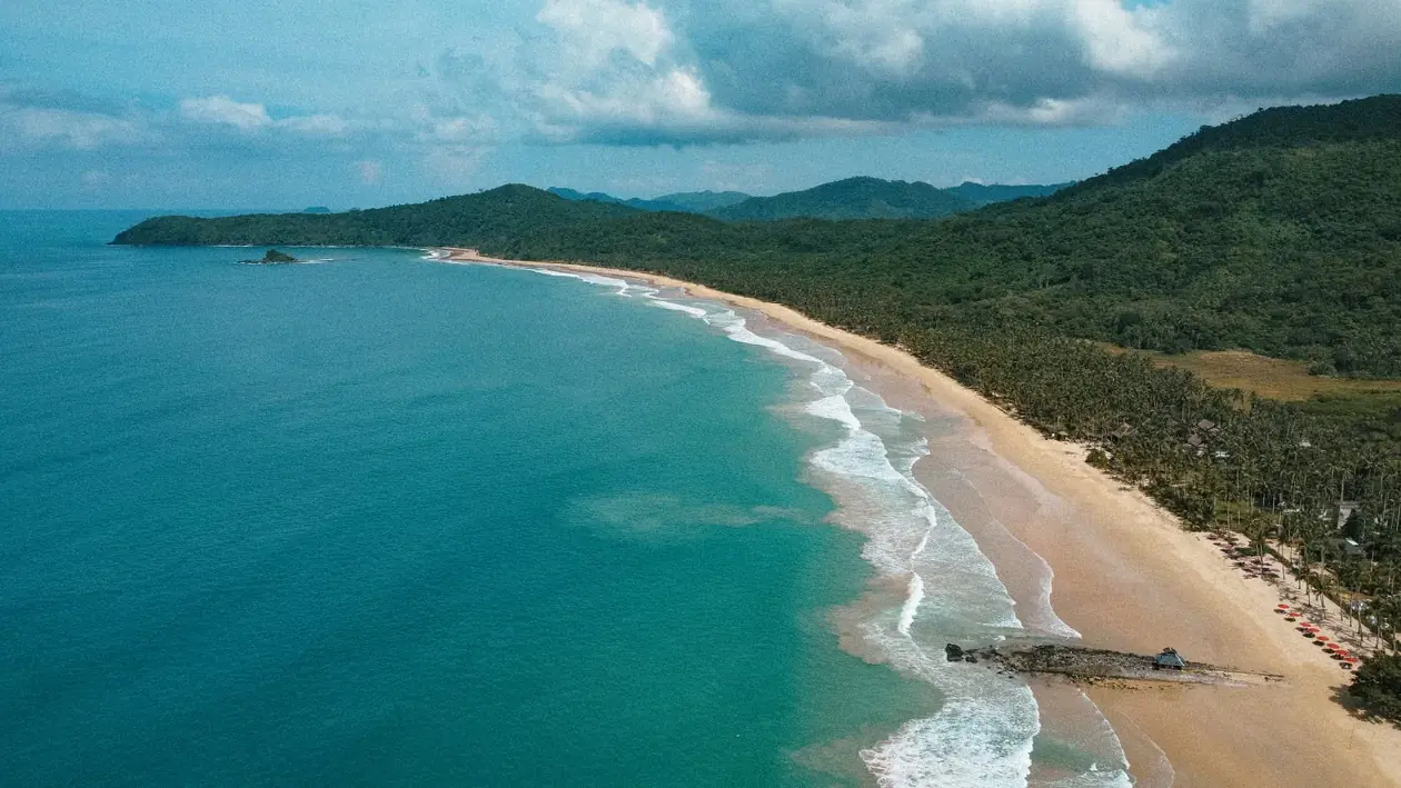 Aerial view of Duli Beach in El Nido, Philippines with turquoise water and a long sandy shoreline.