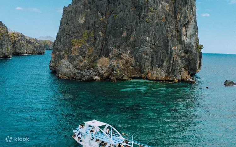 Boat on an El Nido island hopping tour near limestone cliffs.