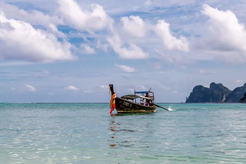 Longtail boat on turquoise tropical sea with limestone cliffs.