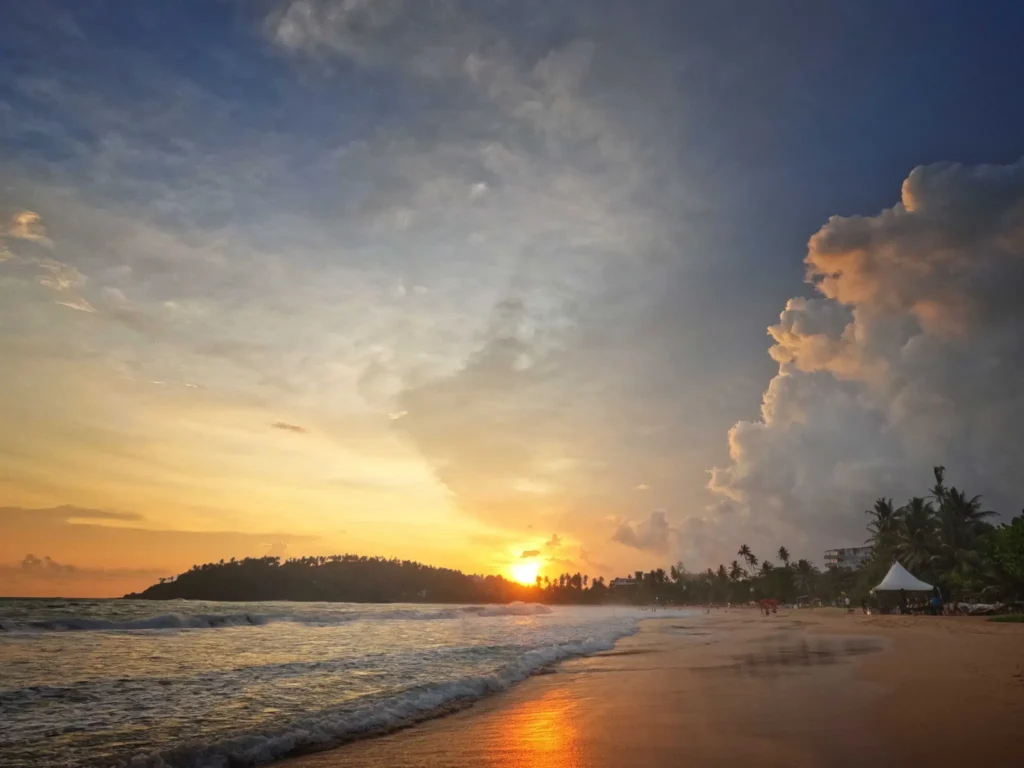 Sunset over Mirissa Beach with waves and dramatic clouds.