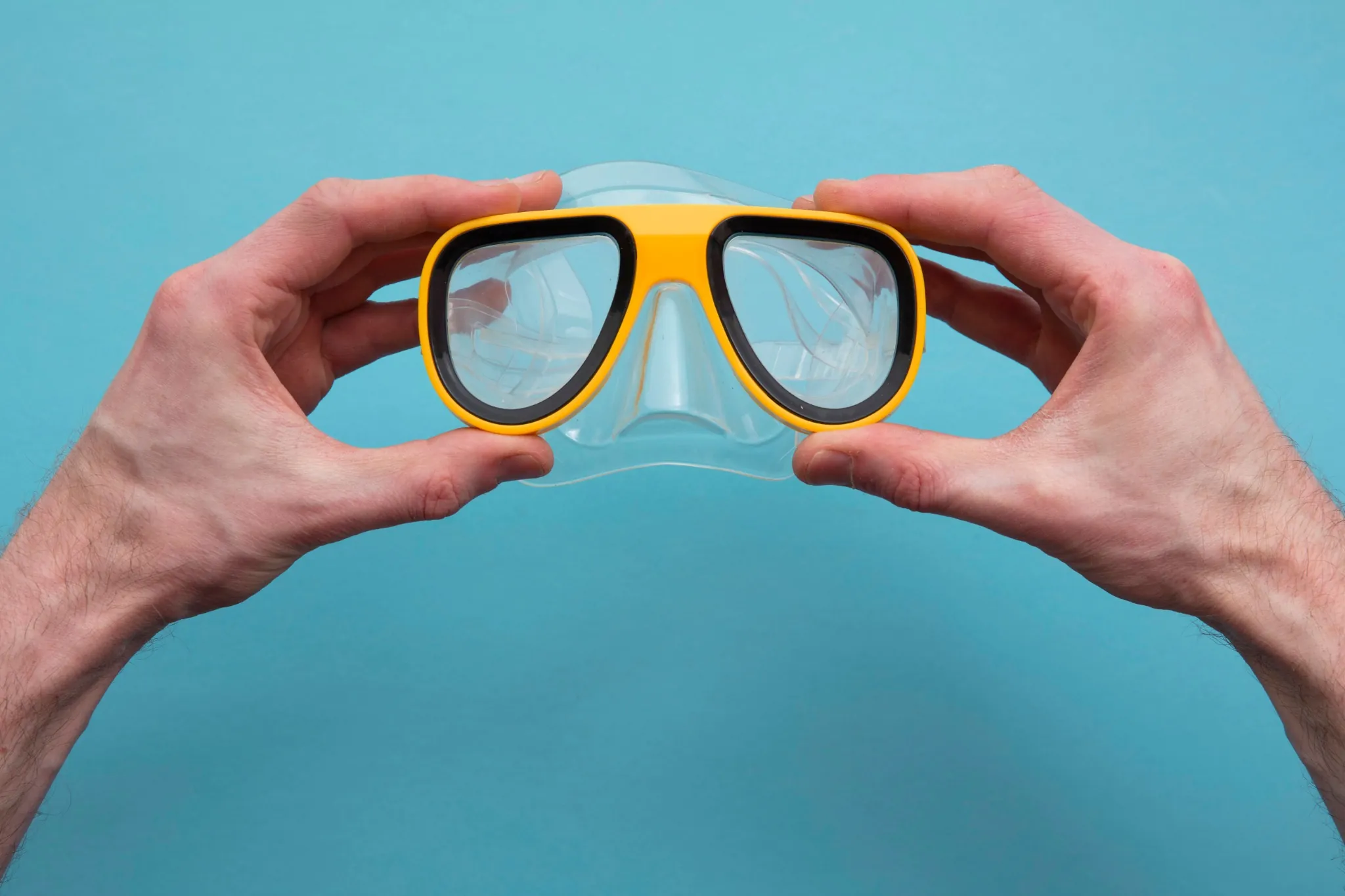 Person holding yellow and black snorkeling goggles against a blue background.