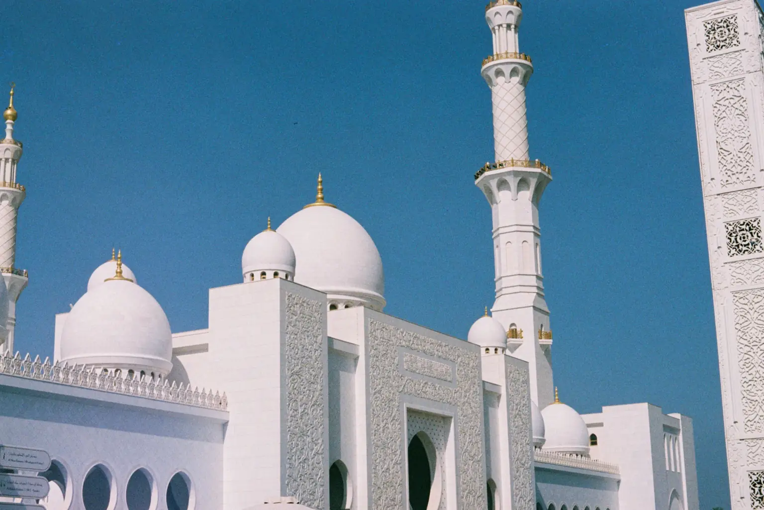 White marble domes and minarets of Sheikh Zayed Grand Mosque in Abu Dhabi beneath a blue sky.