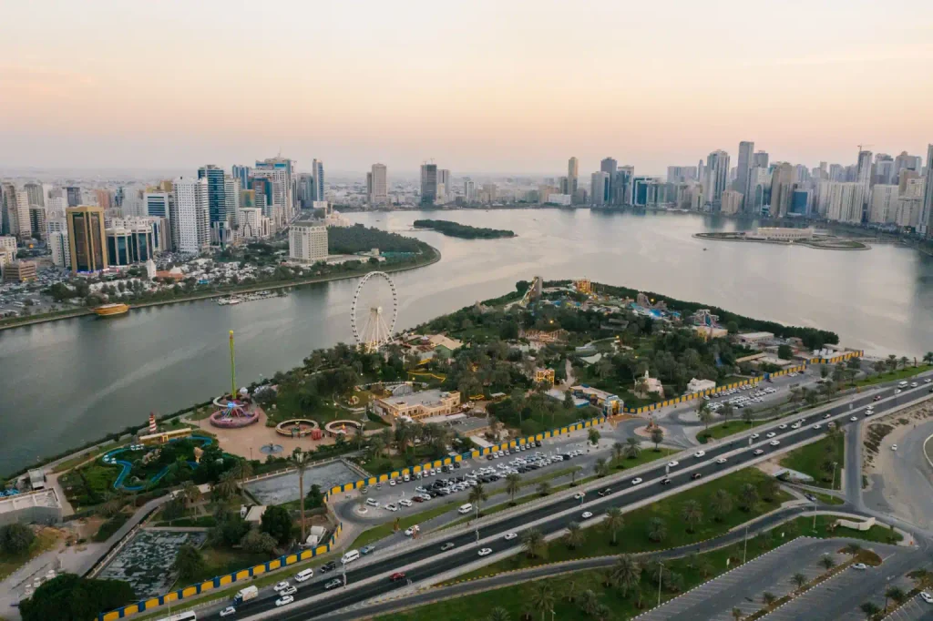 Elevated view of Sharjah’s Khalid Lagoon, waterfront skyline and Al Montazah Parks with a Ferris wheel.